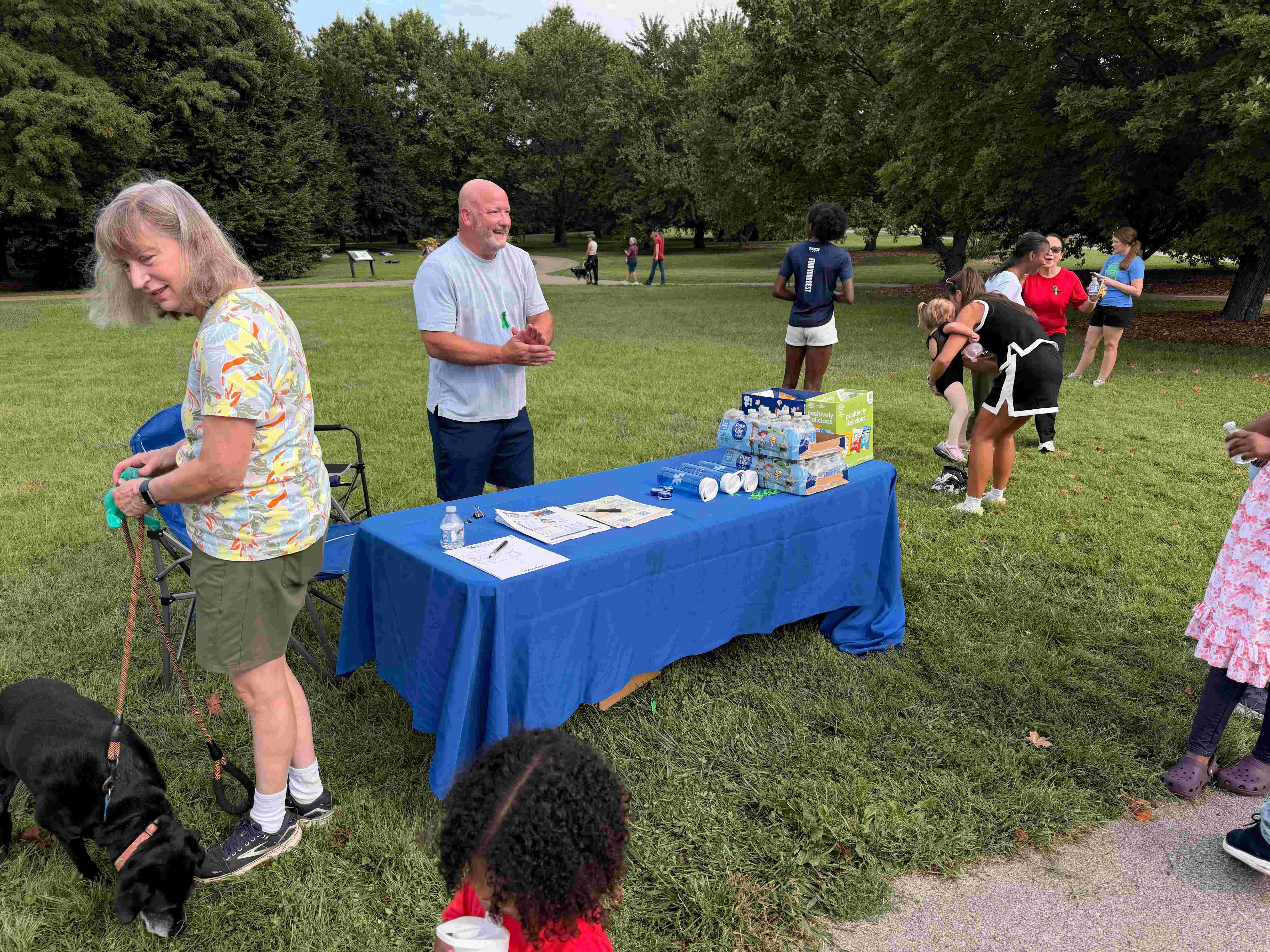 check in table with man attending it and scattered people in the background in a park