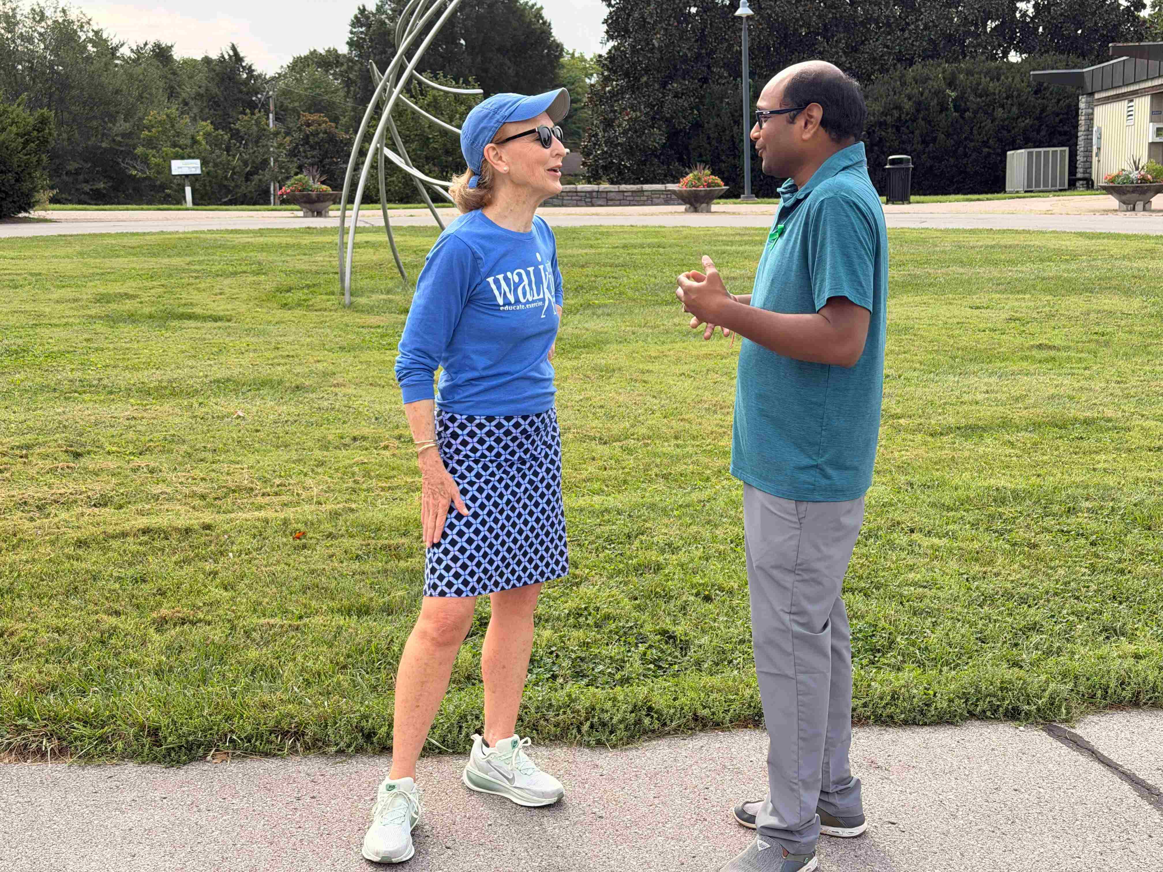 a man and a woman talking in front of grass and metal art structure