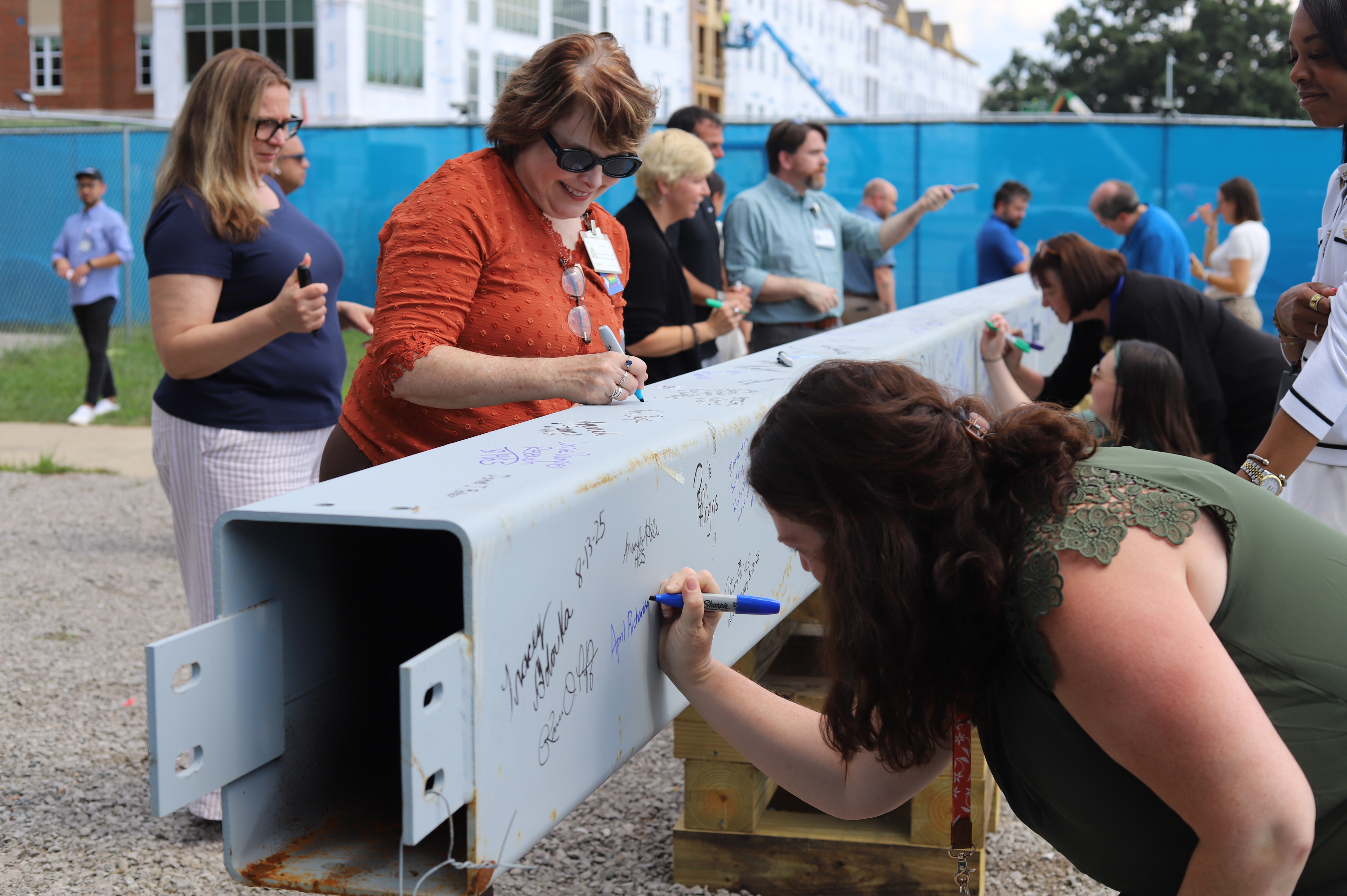  Faculty, staff, learners, and alumni signing a ceremonial beam