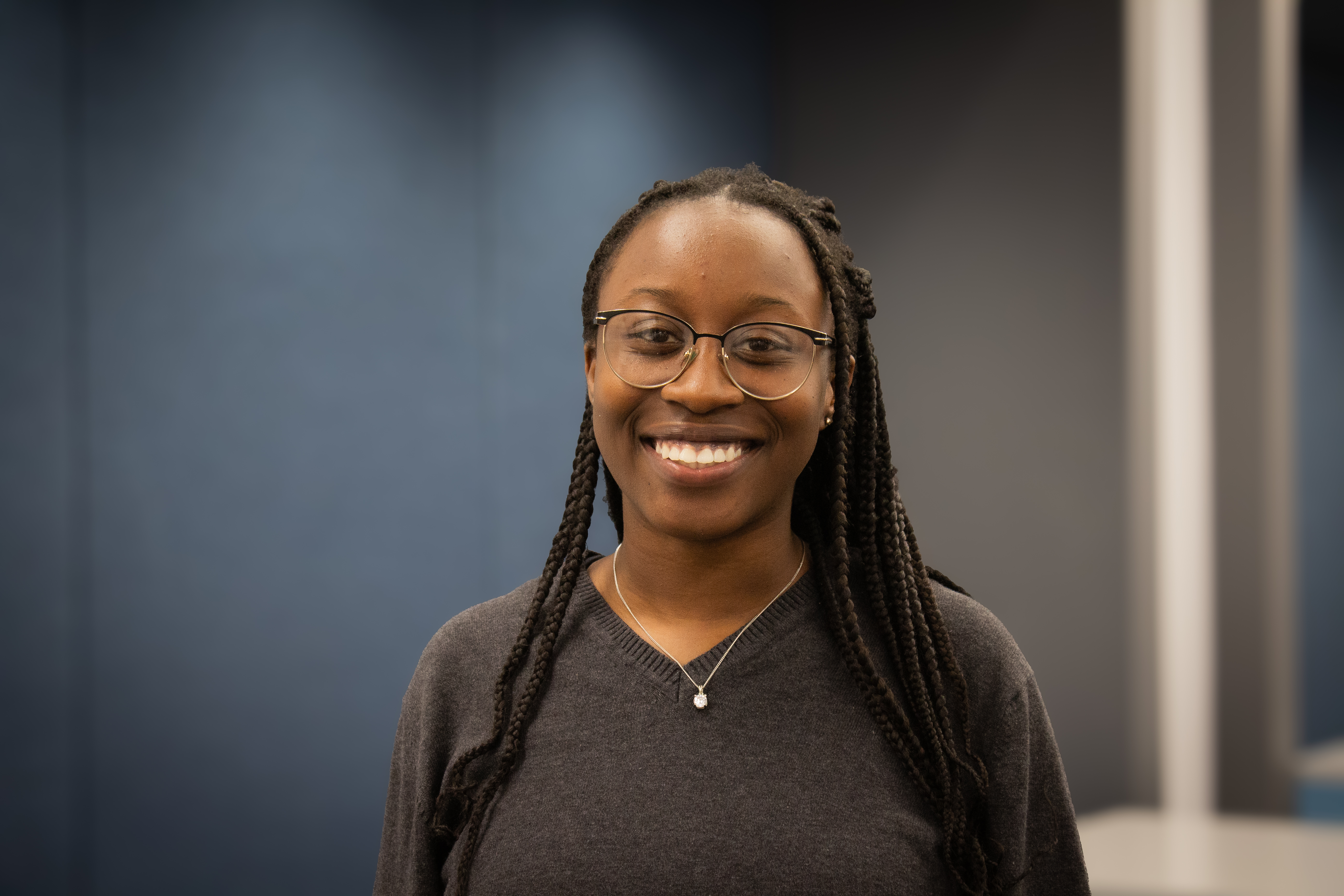 Young lady in black top standing in front of blue background, smiling