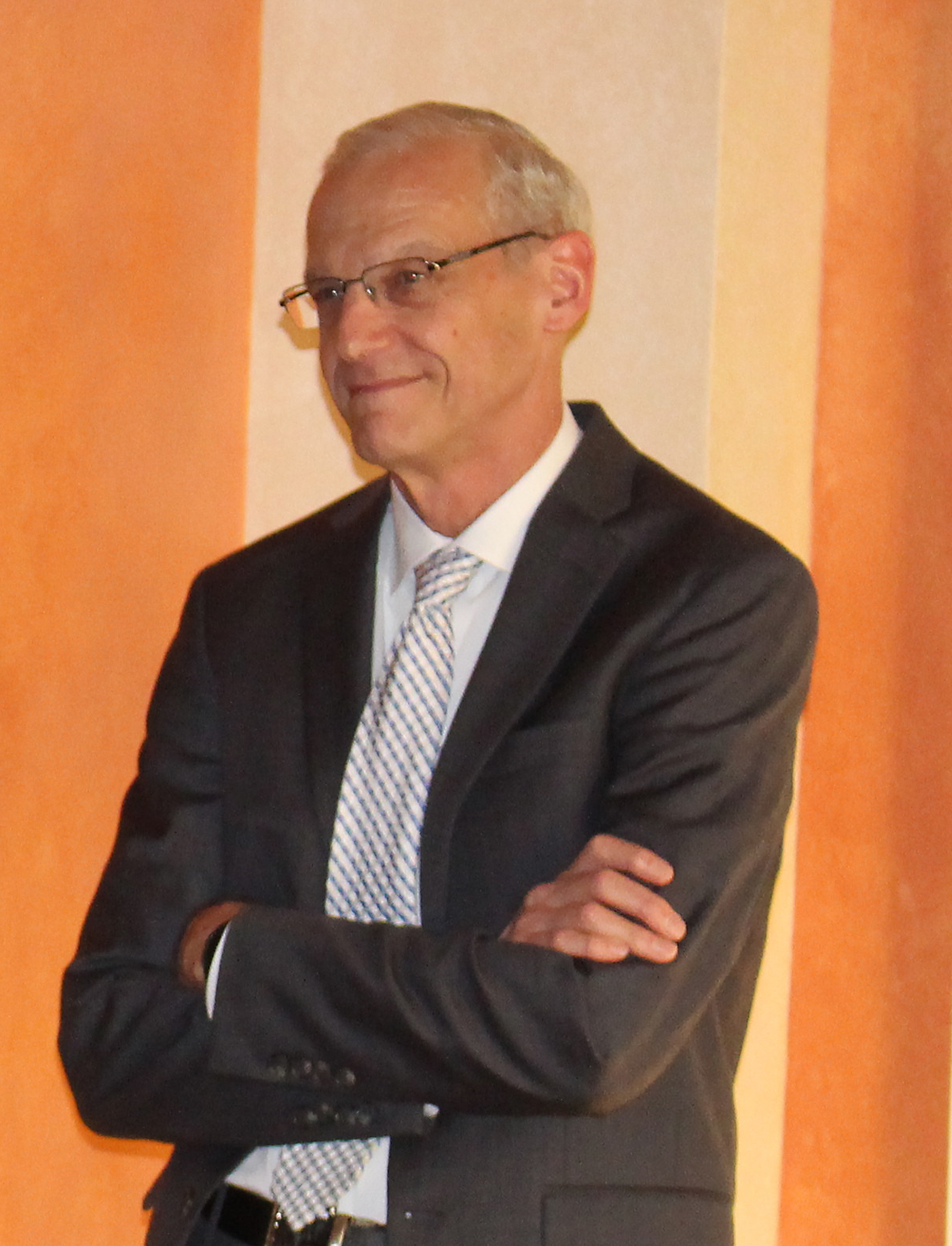 Dr. Endean is dressed in a gray suit and leaning against a salmon-colored wall