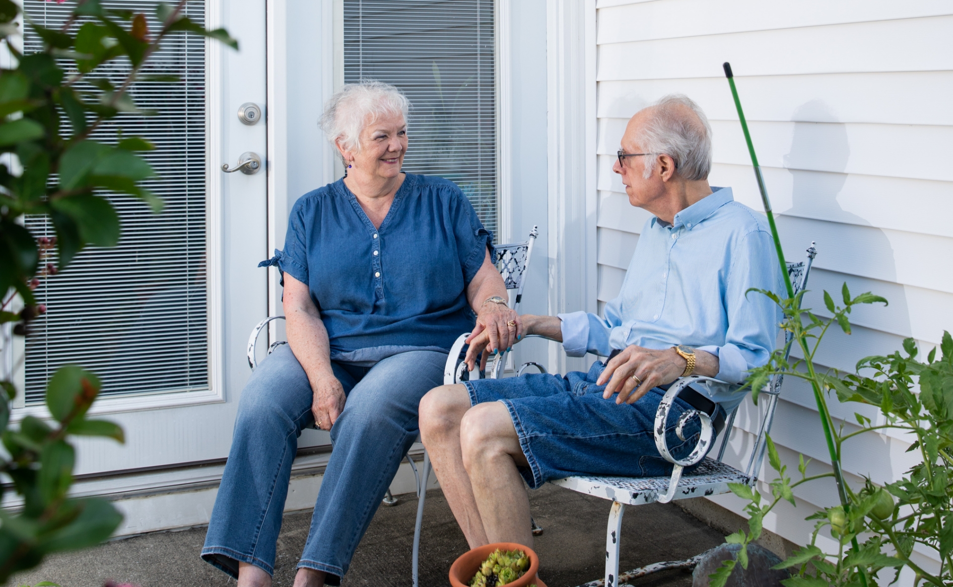 two elderly people sit together outside their house 