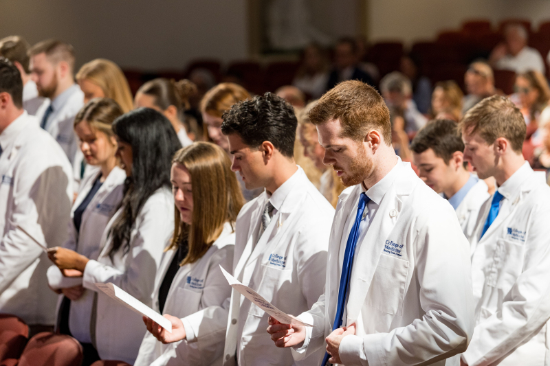 A large group of students wearing white coats recite a pledge during their white coat ceremony