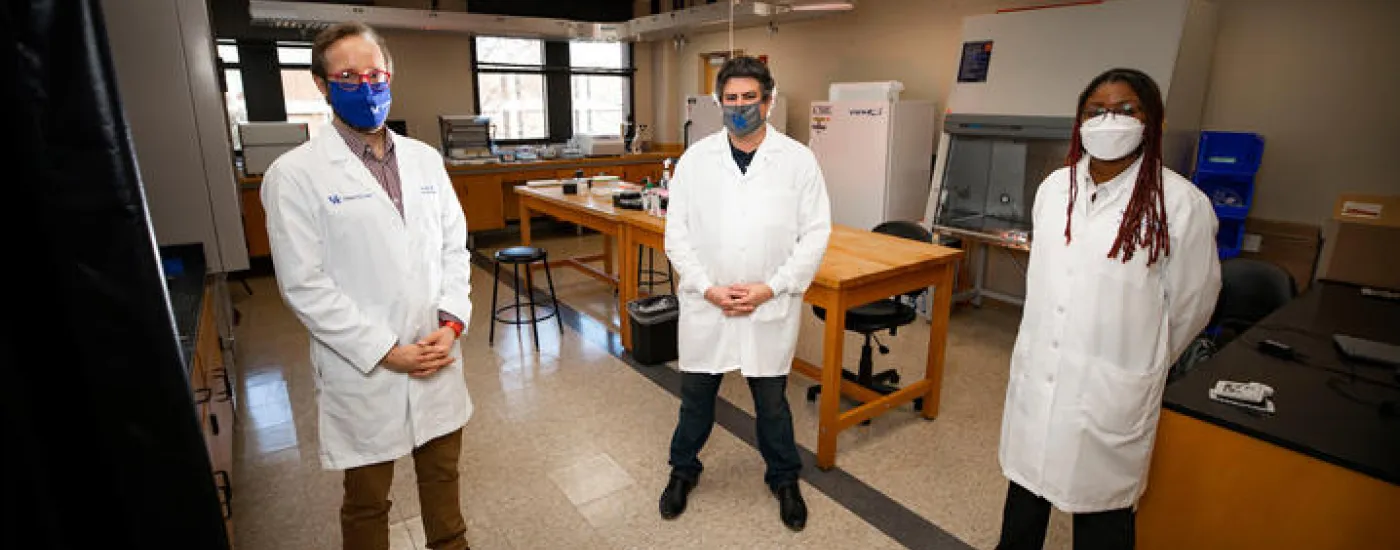 3 researchers standing apart with a laboratory in the background