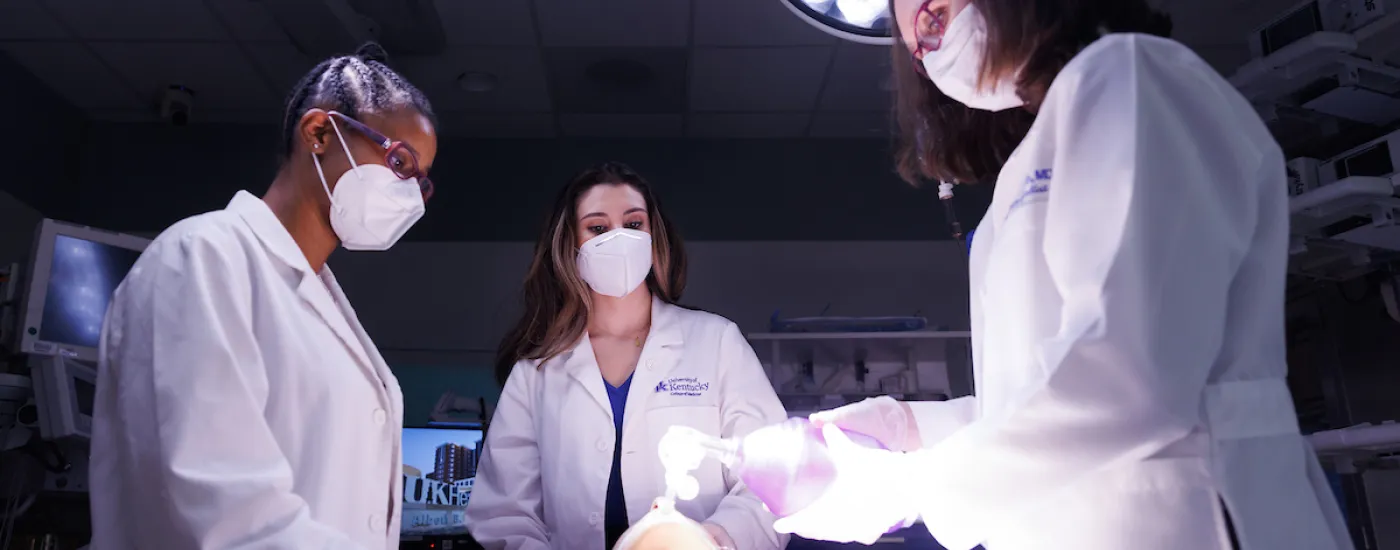 3 medical students in an exam room with a medical dummy