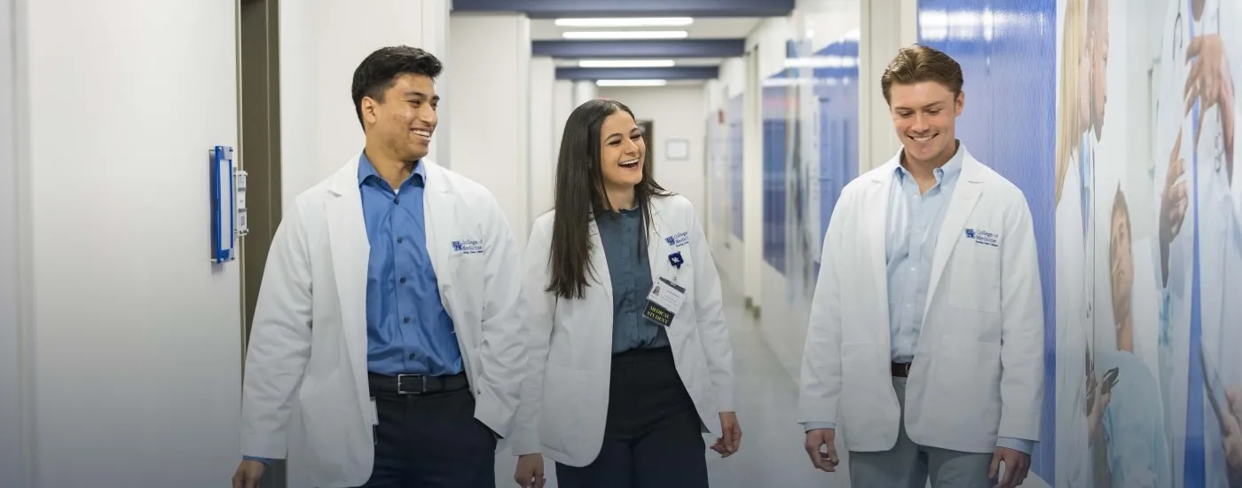 Three medical students walking together down a hallway with their white coats