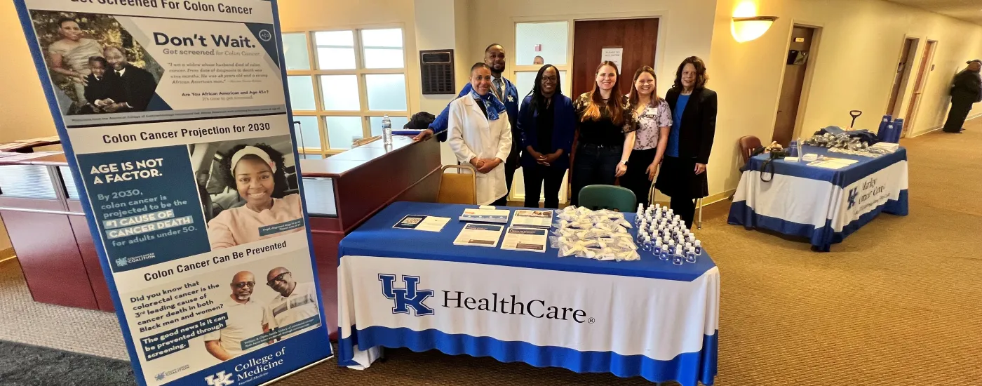 A group of people stand at a table with a table cloth that reads "UK HealthCare"