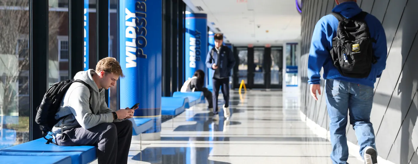 Hallway at the UK Gatton Student Center with one student seated on a bench and one walking