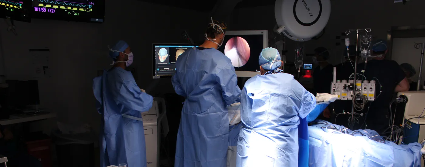 A dark room with three surgeons in scrubs performing surgery