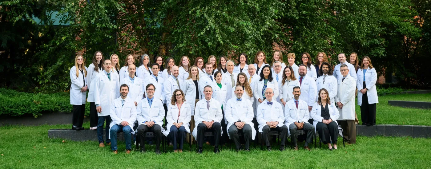 A group picture of UK Otolaryngologists, Audiologists, and APPs smiling in their white coats outside. 