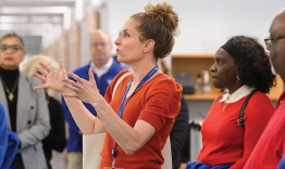 A woman gesturing while speaking to a large group of people.