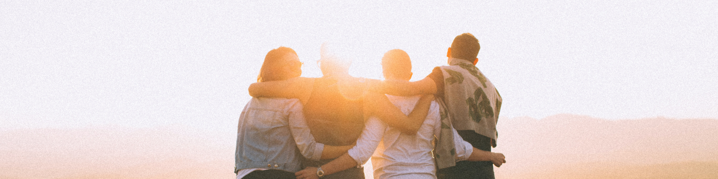 4 individuals arms entwined standing side-by-side with a sunset in background