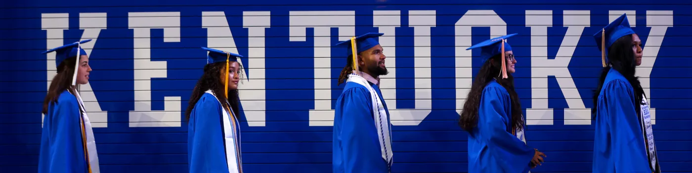 Graduates walking in front of a wall with "Kentucky" painted on it. 