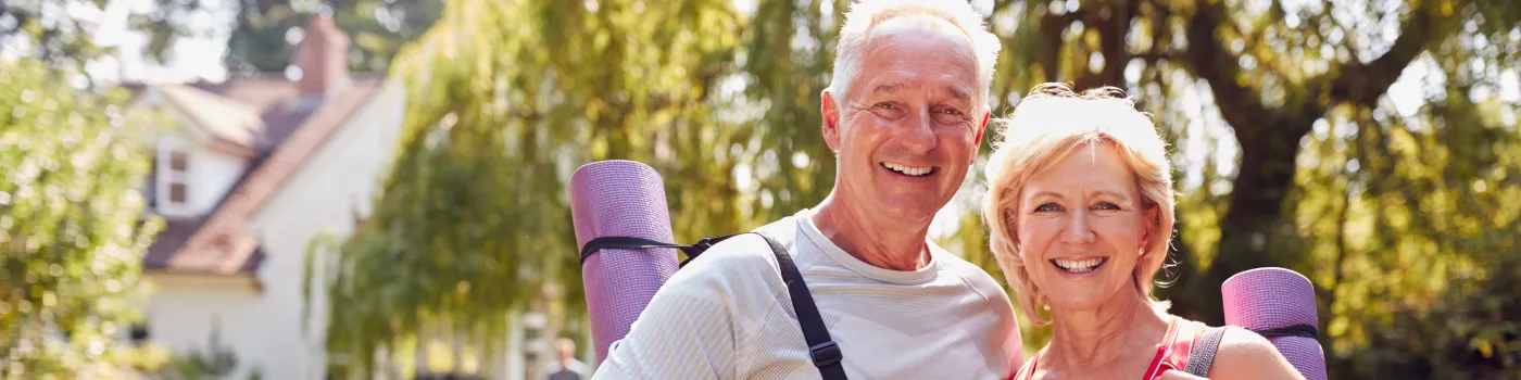 Senior couple hugging while wearing yoga mats on their backs. 