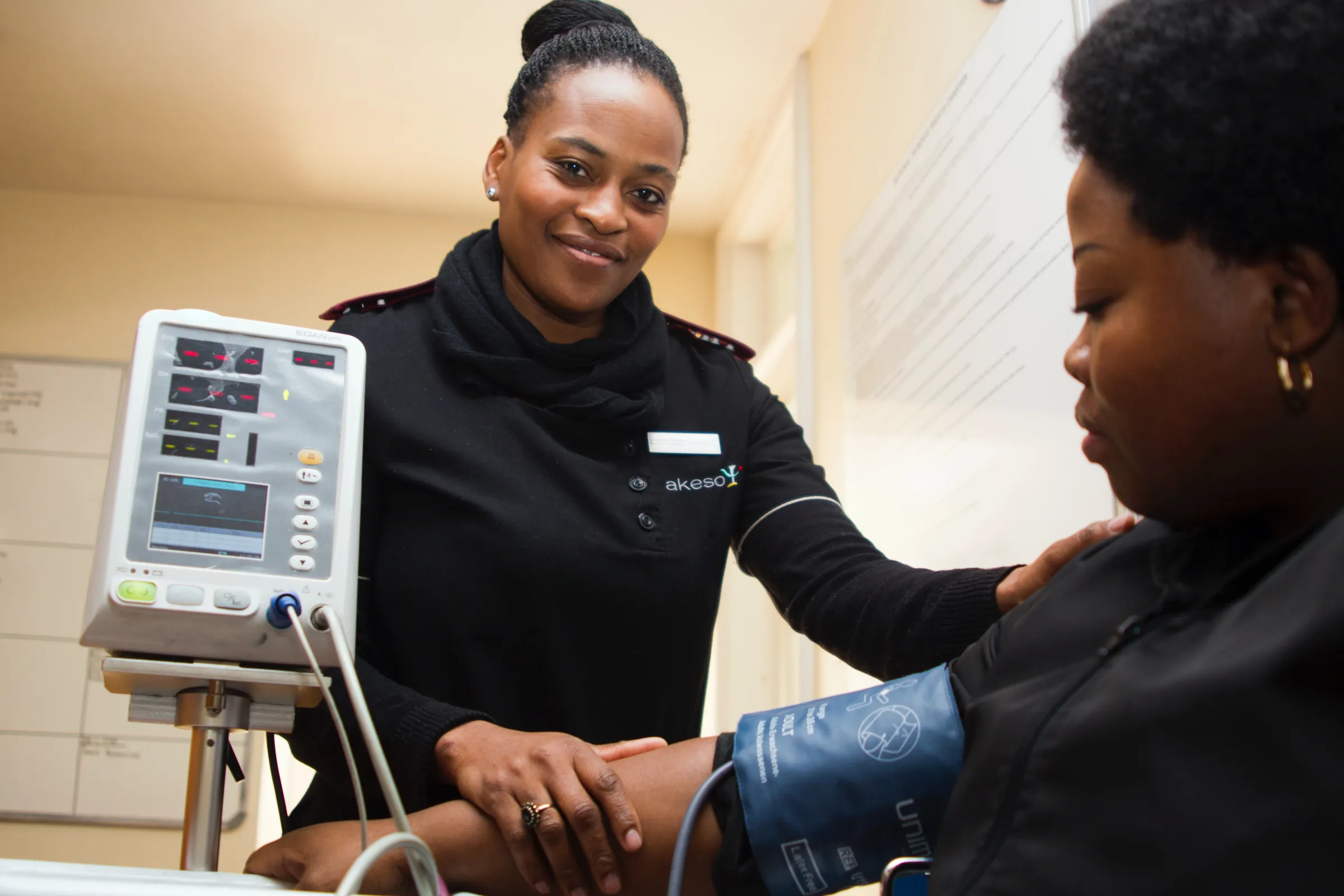 2 people:  one a provider and one sitting in a chair with a blood pressure monitor