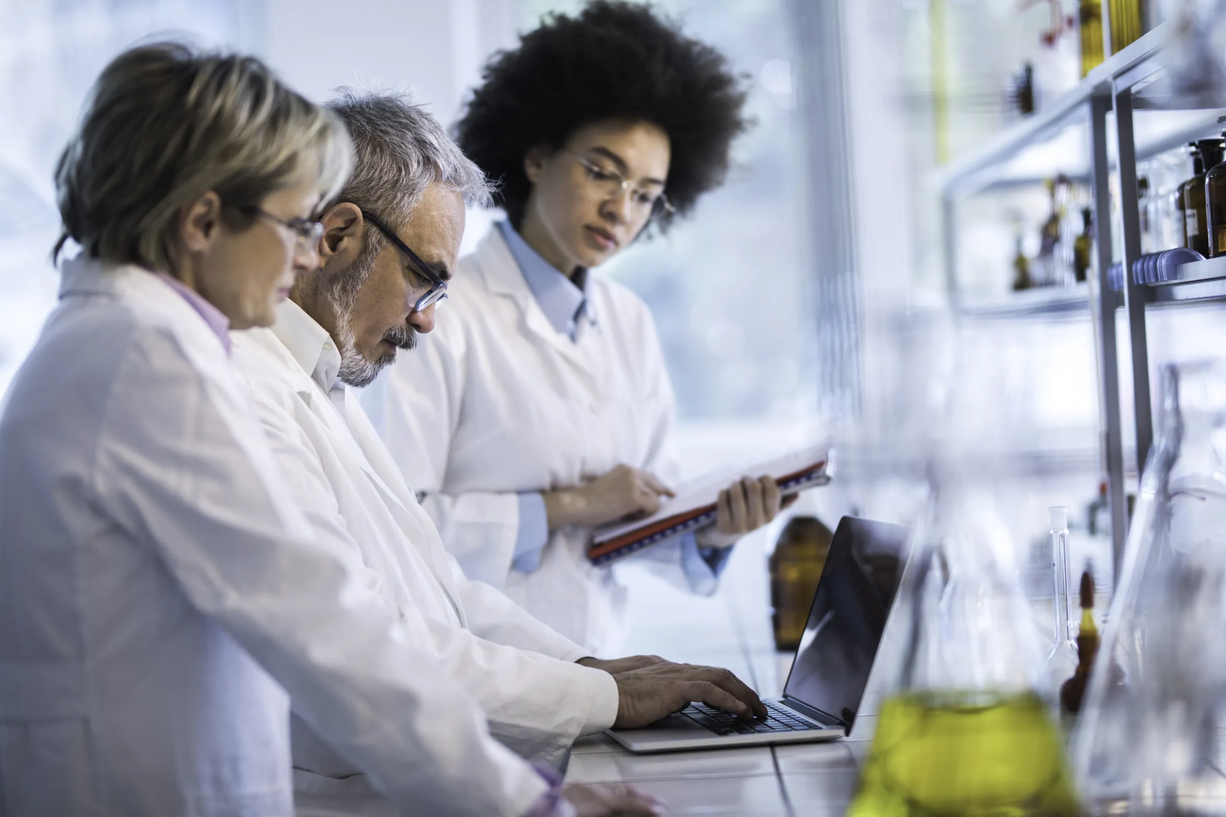 3 researchers looking down at a computer; laboratory in background