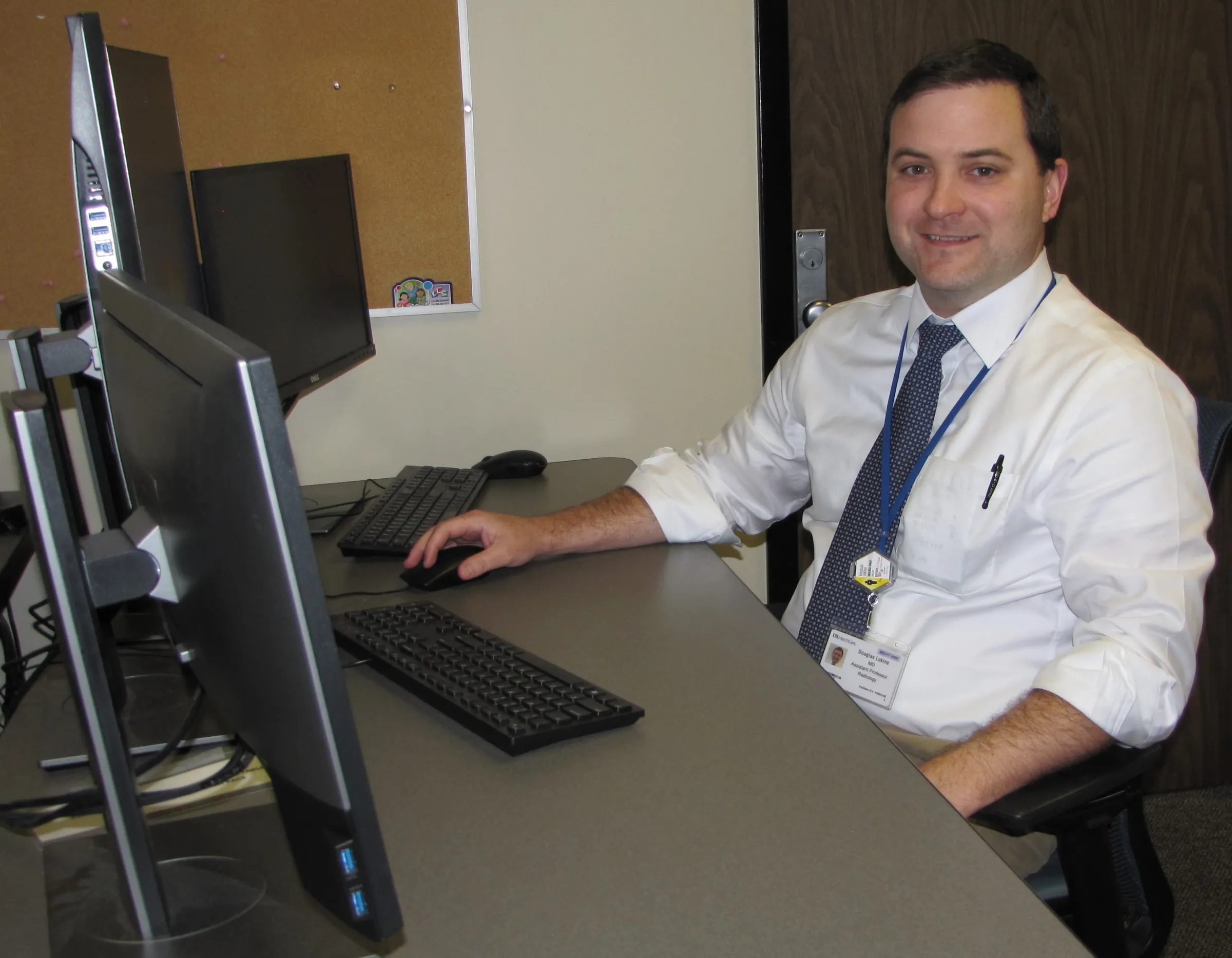 Dr. Douglas Lukins sitting at a desk with two monitors in front of him