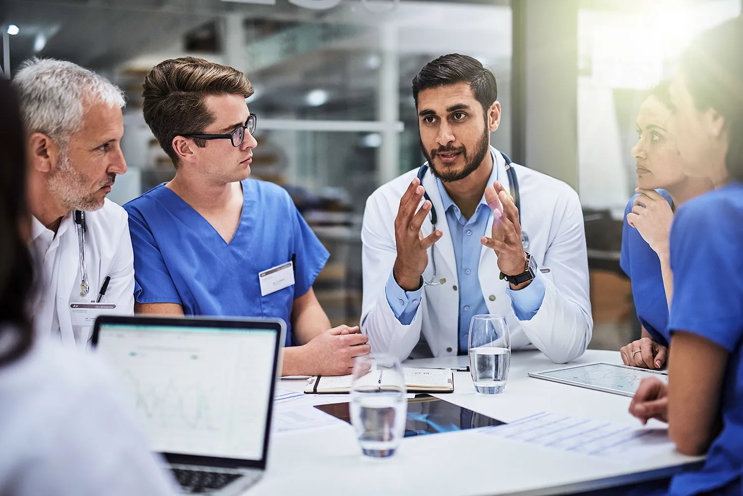 group of medical professionals sitting at a table discussing; water glasses and computers also on table