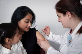 provider giving vaccine to person; child in person's lap