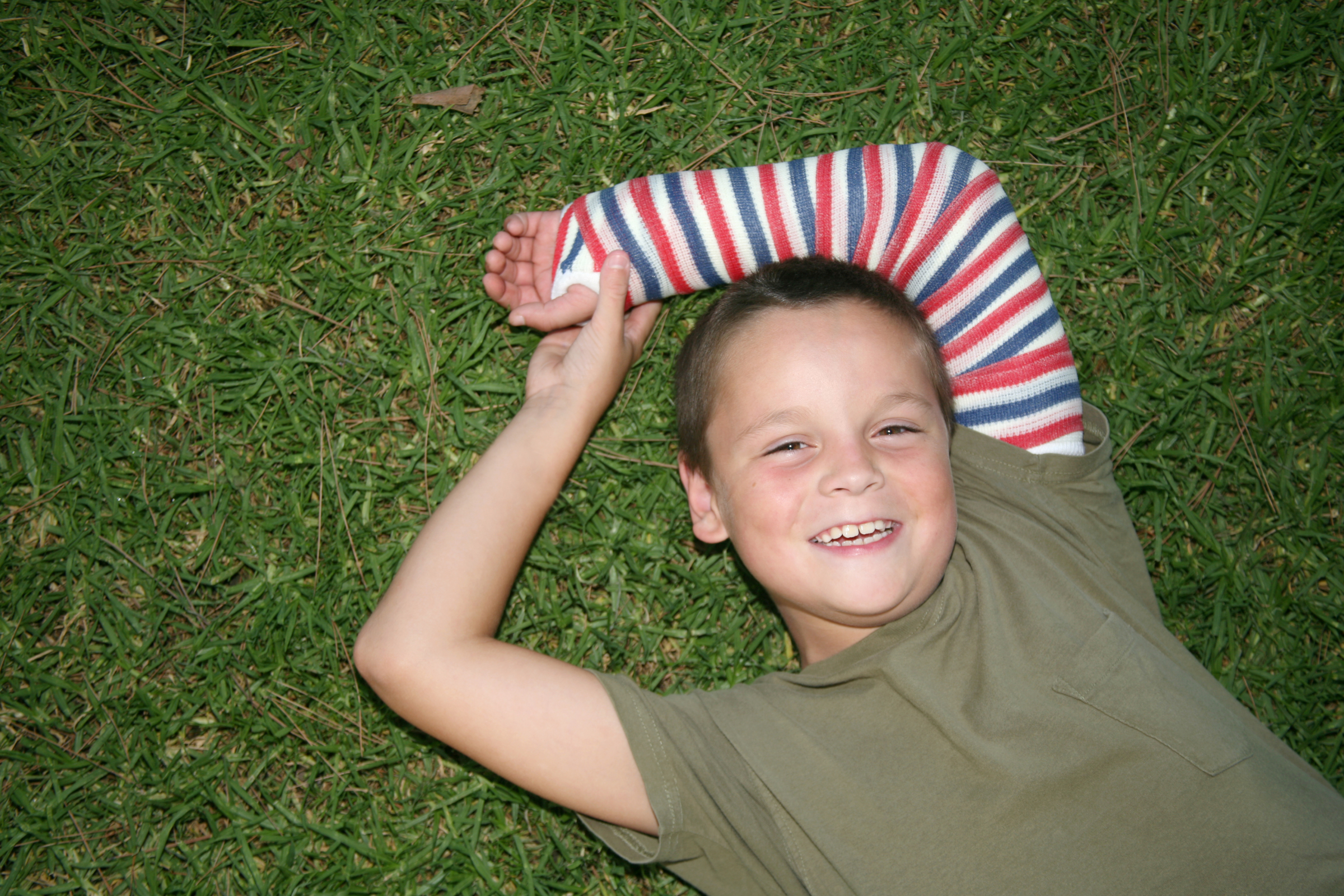 kid laying in the grass with a multi-colored cast on arm