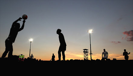 night soccer game, players outlined against setting sun horizon