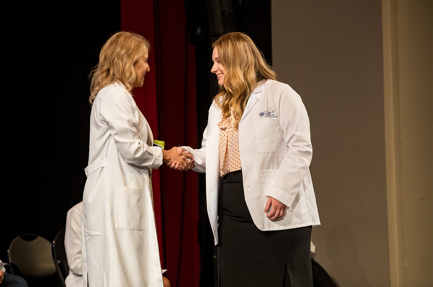 new student shakes hands with faculty member on stage at white coat ceremony