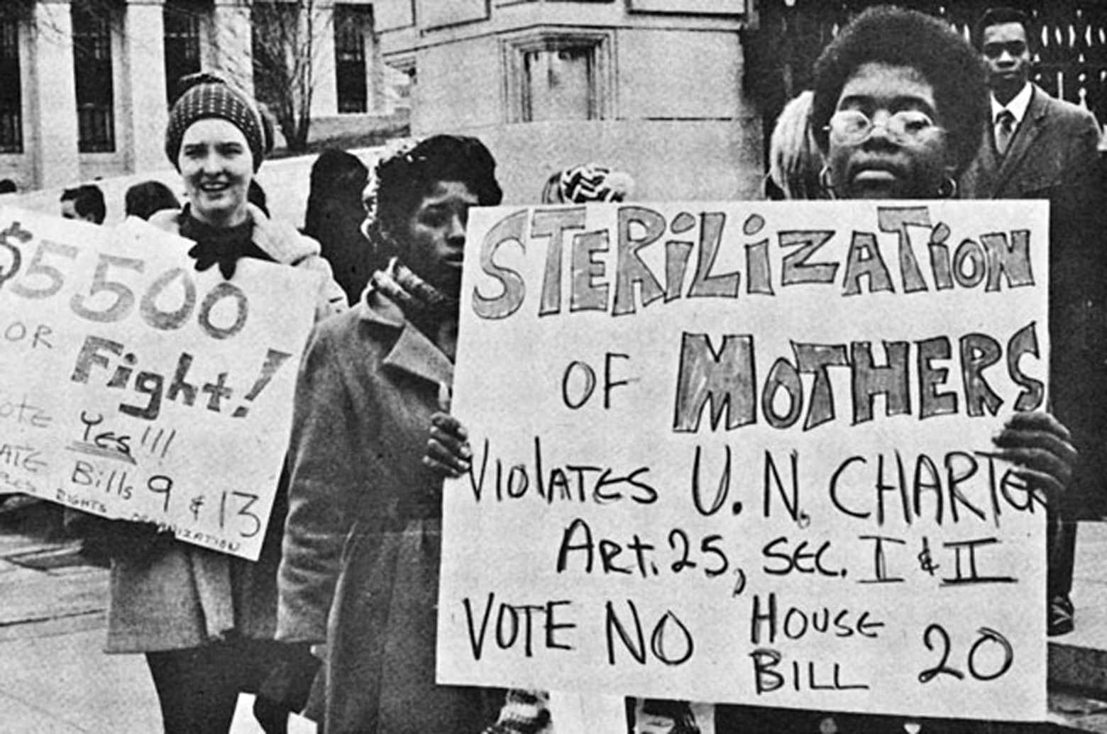a black and white photo of a woman holding a protest sign against forced sterilization in the US