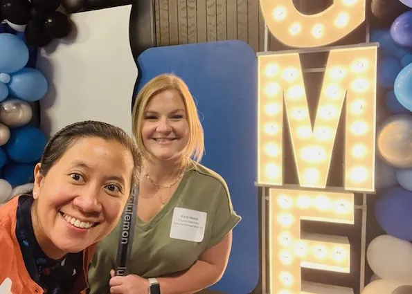Dr. Sithisarn (PD) and Kerbi Meade (PC) in front of a decorative GME light sign.