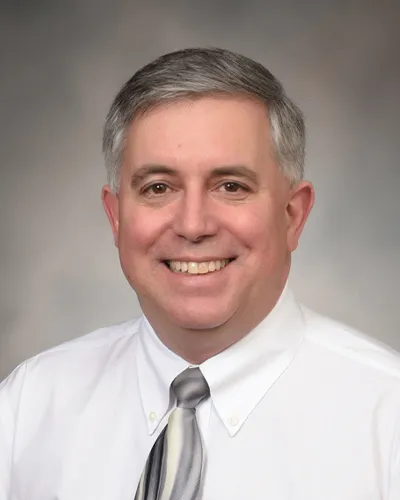 A picture of Dr. Simon Fisher in a white collared shirt. He is smiling.
