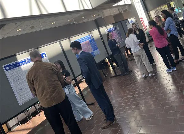 A group of people gathered to see poster presentations in the entry hall of a building.