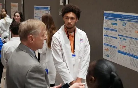 A man appraises another man's poster while he stands by in a white coat