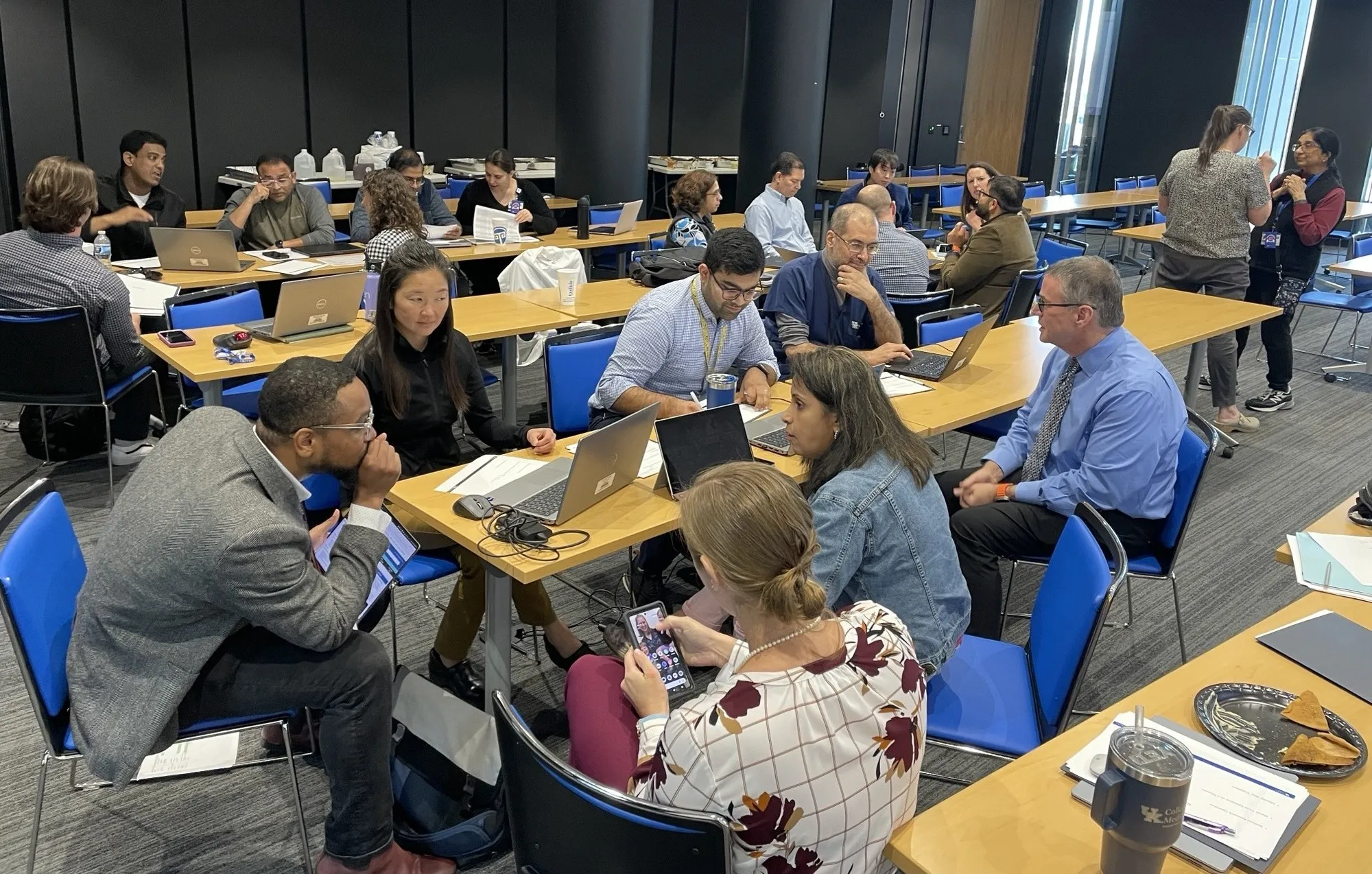 Several people at long, wooden tables work on laptops