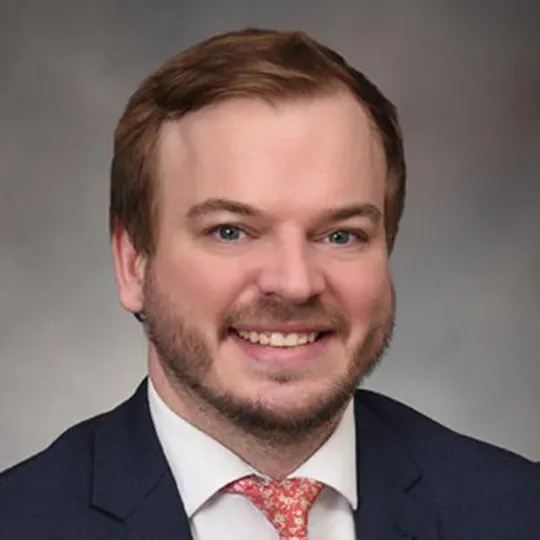 Andrew Smith, a red headed man, wearing a black suit and orange tie.