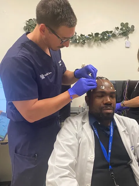 Picture of Dr. Paul Wilkerson practicing placing EEG electrodes on another fellow.