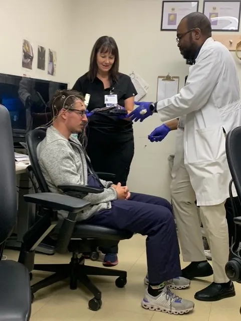 Picture of Dr. Fatai Akemokwe practicing placing EEG electrodes on a fellow. Include in the photo is an EEG lab technician.