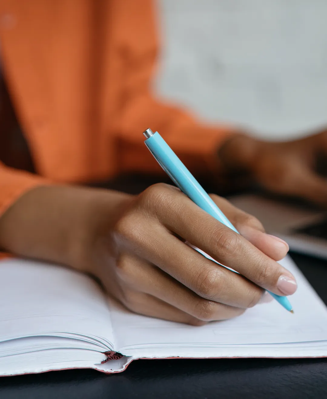 A hand writes with a blue pen in a notebook