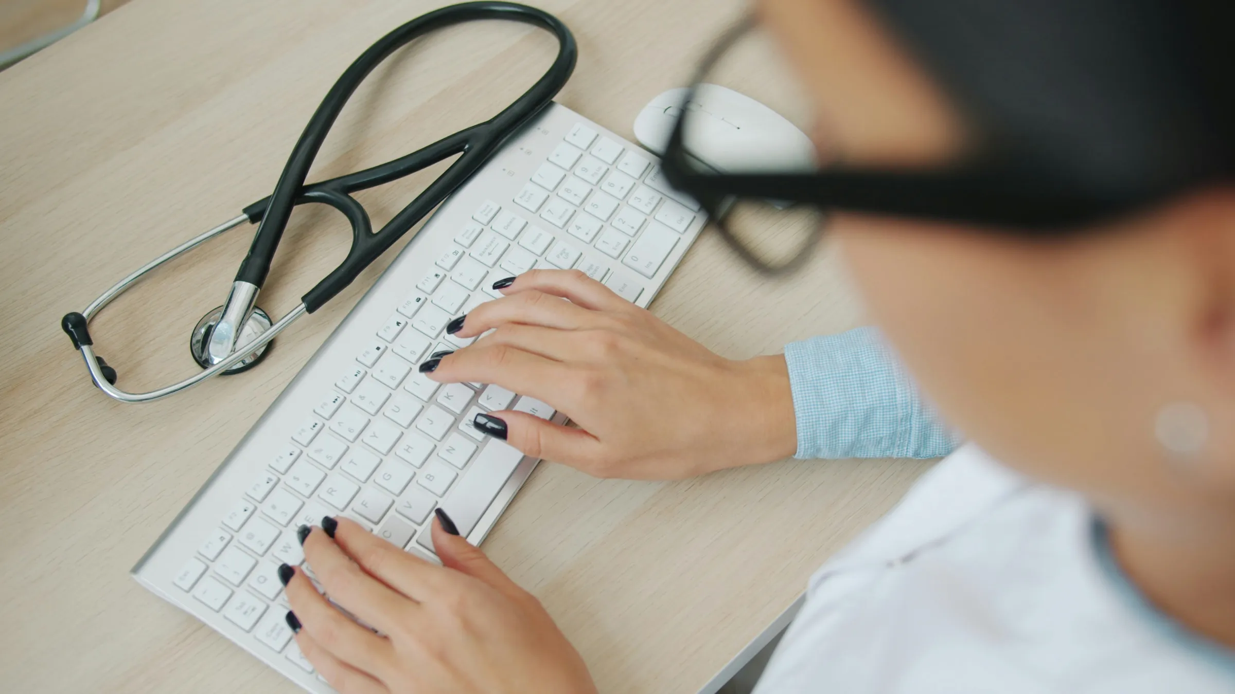 An individual types on a keyboard. There is a stethoscope on the desk as well.