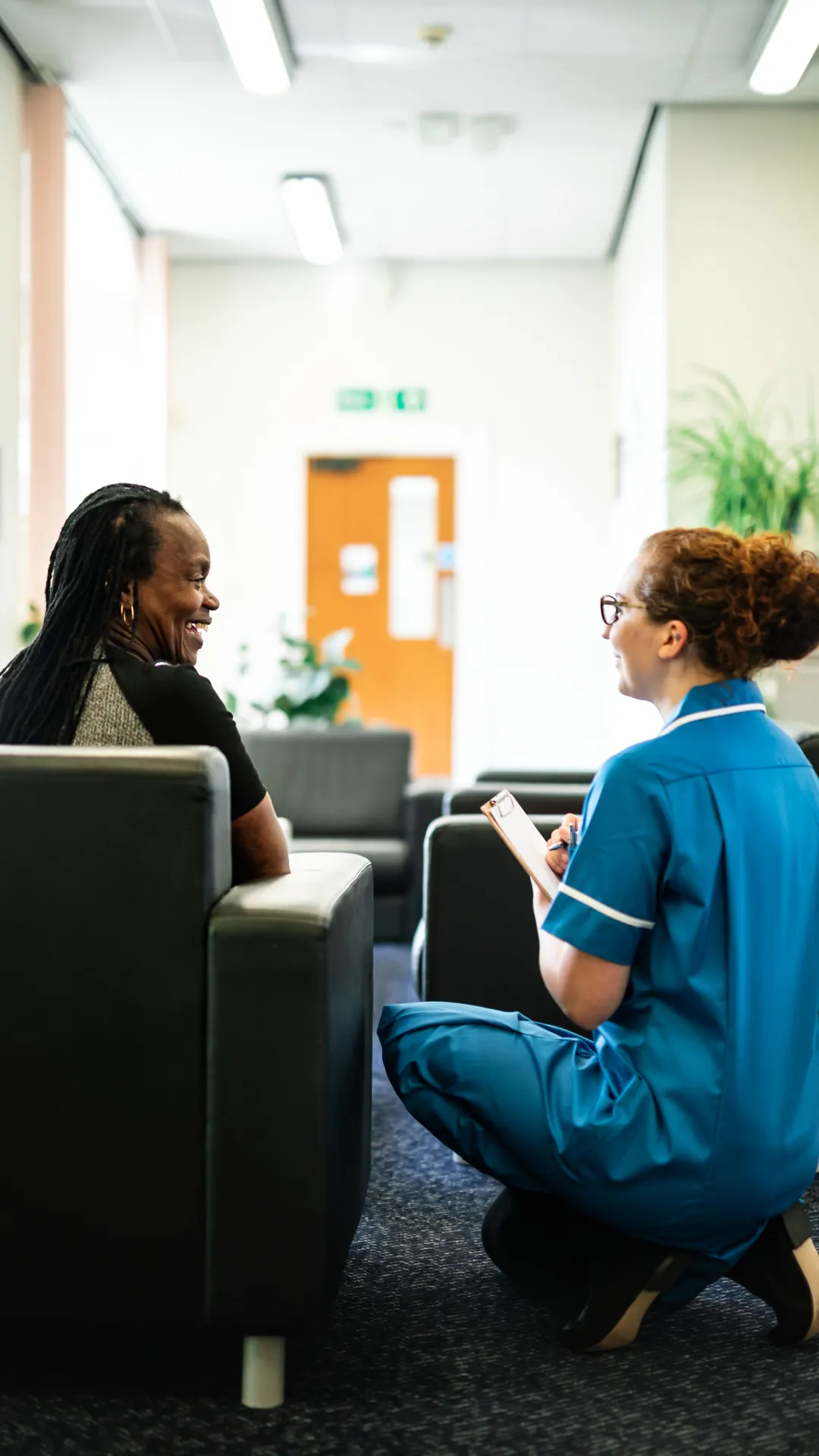 A nurse squats to speak with a patient sitting in a chair