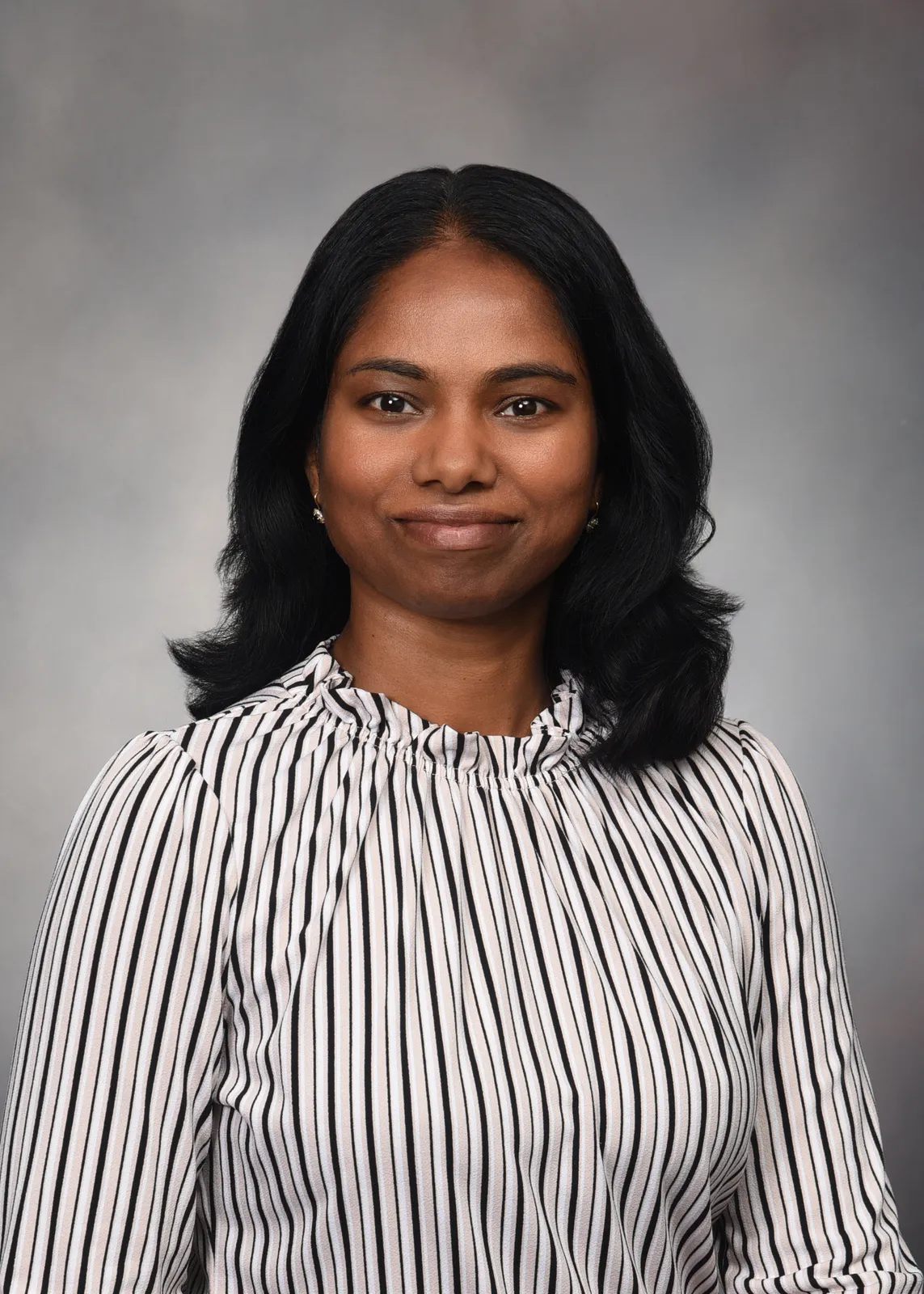 Sathya Velmurugan poses for a headshot in a striped blouse