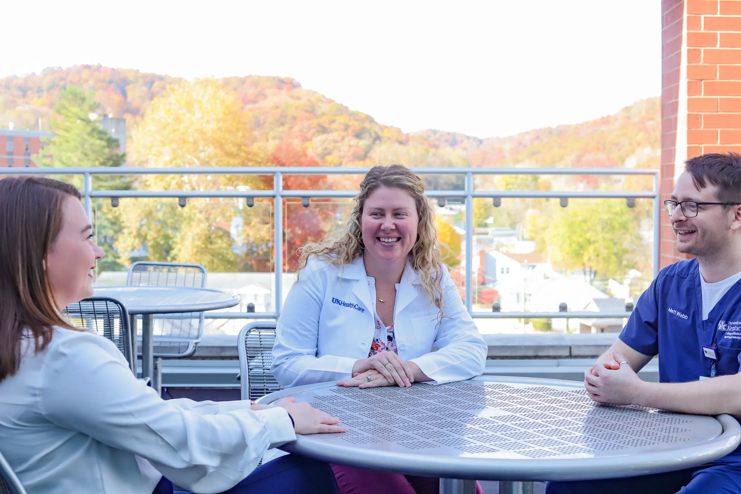 a faculty member with a resident and medical student around a table in coversation