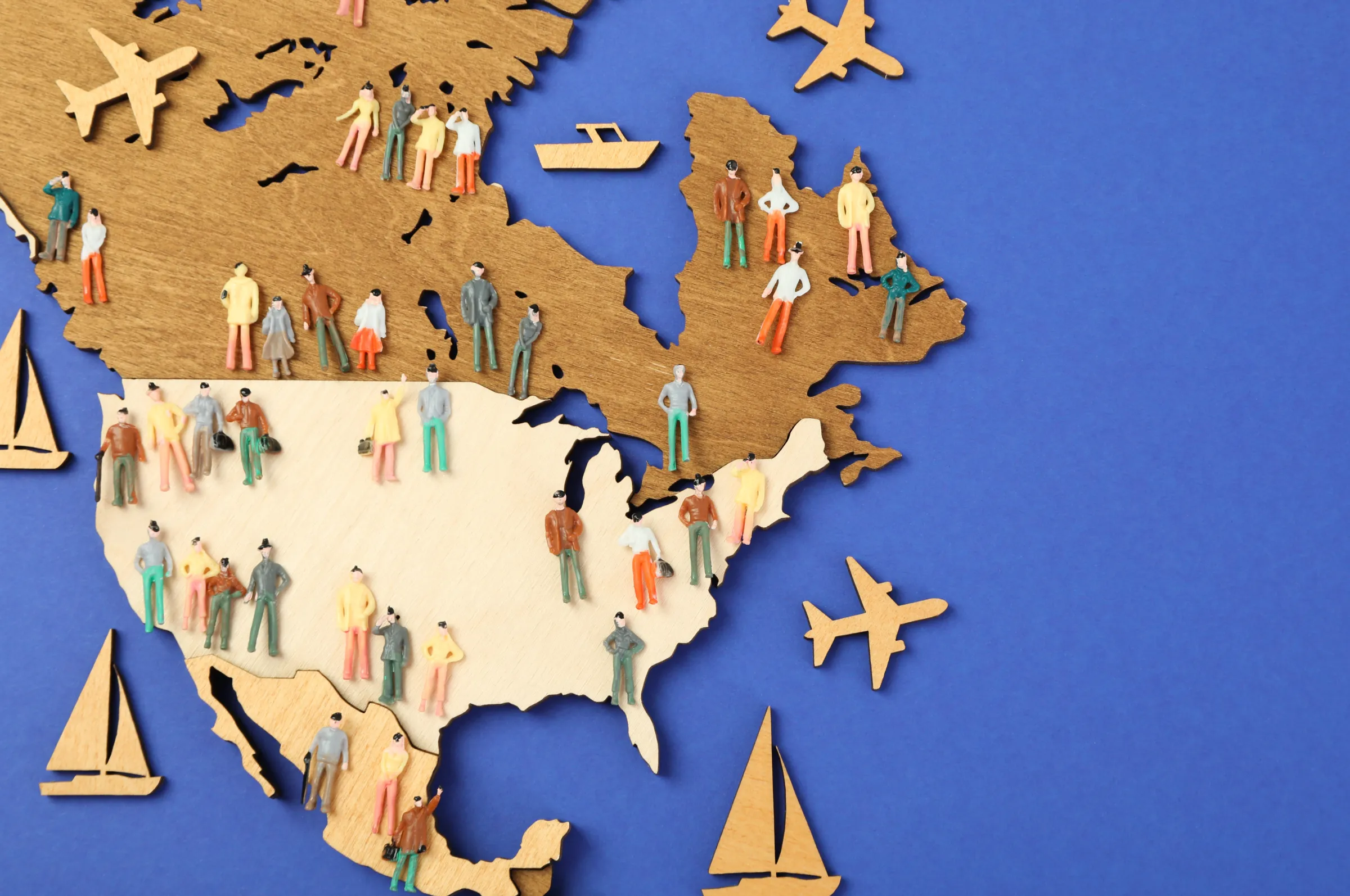 A navy background with a wooden map of the North America continent with colorful people scattered across. 