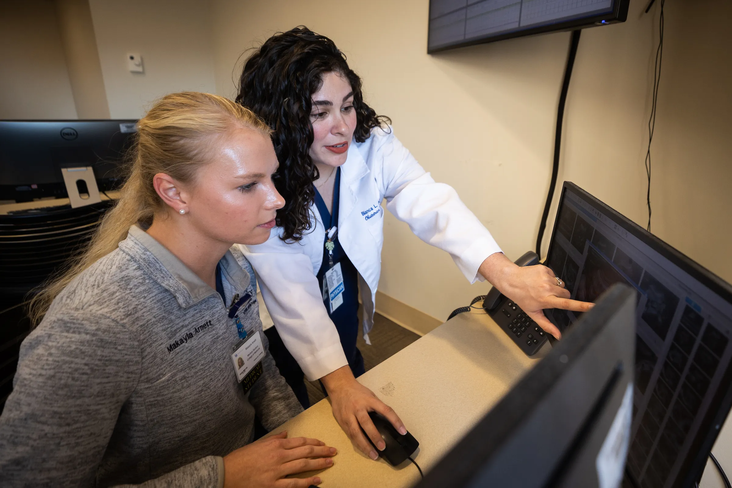 A female student being guided through a computer process by a woman in a white coat.