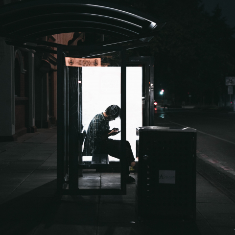 man waiting at a bus stop while on his phone.