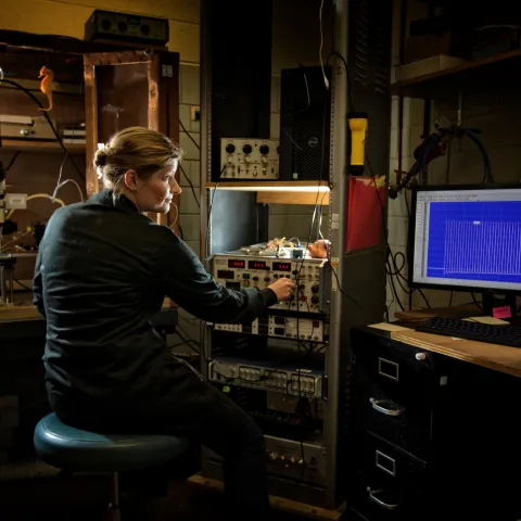 researcher surrounded by lots of laboratory equipment, screens, and wires
