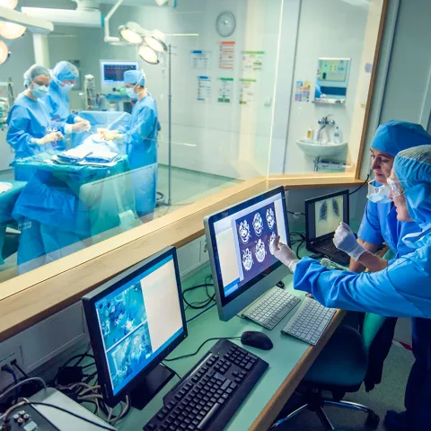 2 providers looking at a screen while surgery is being completed on the other side of a glass divide