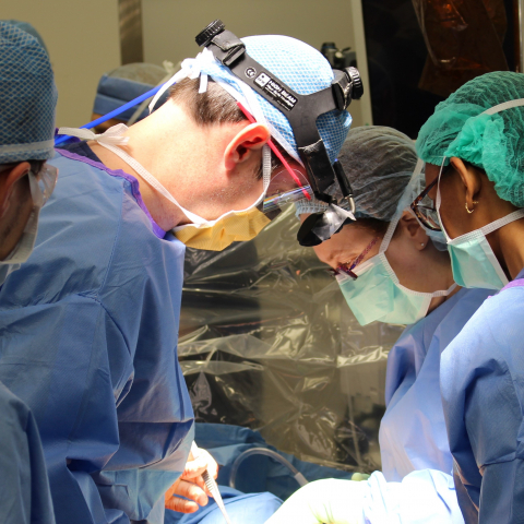A scrubbed surgical team in the operating room huddle together closely during an operation. 