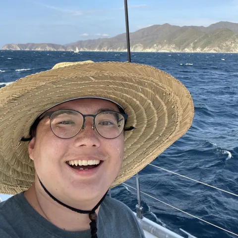 Resident Jaycob Avaylon wearing a sun hat smiling on a boat with the ocean in the background. 