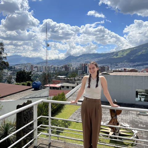 Emily Ranseen leaning against a balcony, with a scenic view of mountains behind her.