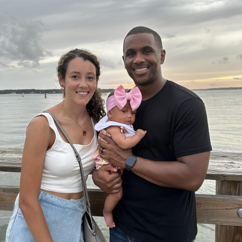 Kendall Noble-Halcomb with her husband and baby girl, standing by the sea.