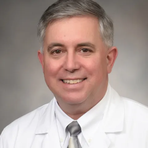 A picture of Dr. Simon Fisher in a white collared shirt and white coat. He is smiling.